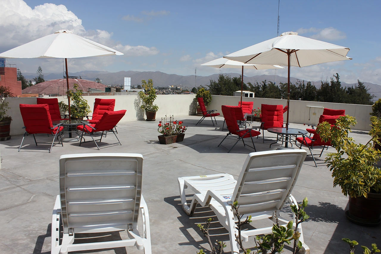 Terraza con tumbonas blancas y sillas rojas con sombrillas